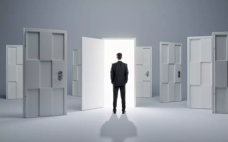 A figure among many closed doors, with one open onto light