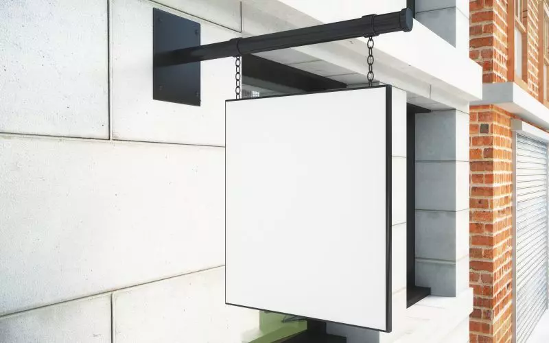 A blank hanging shop sign on a wall bracket