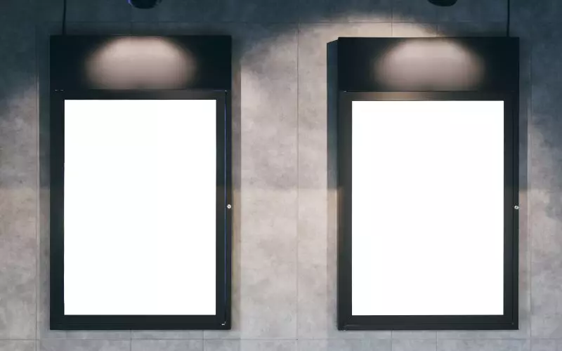 Two empty picture frames lit on a gallery wall
