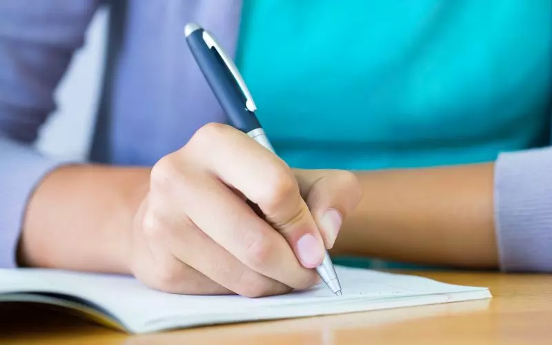 A person writing notes with a pen at a desk