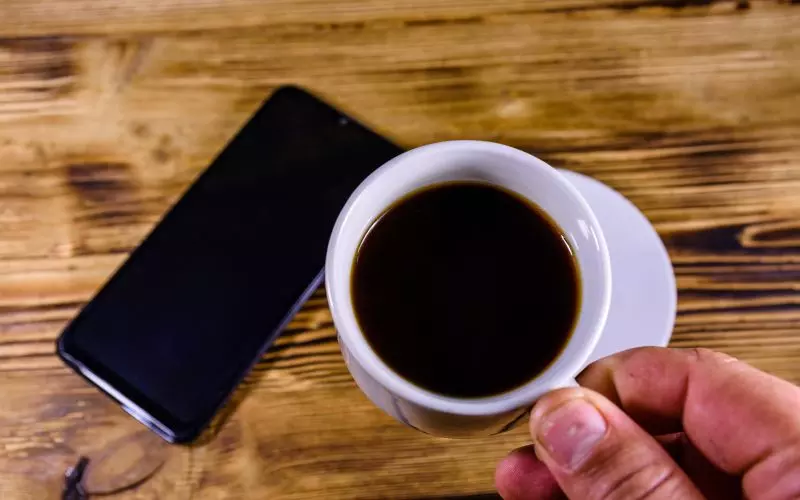 A phone and a coffee cup on a wooden desk