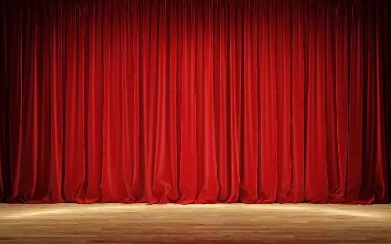 A red theater curtain closed over a lit wooden stage