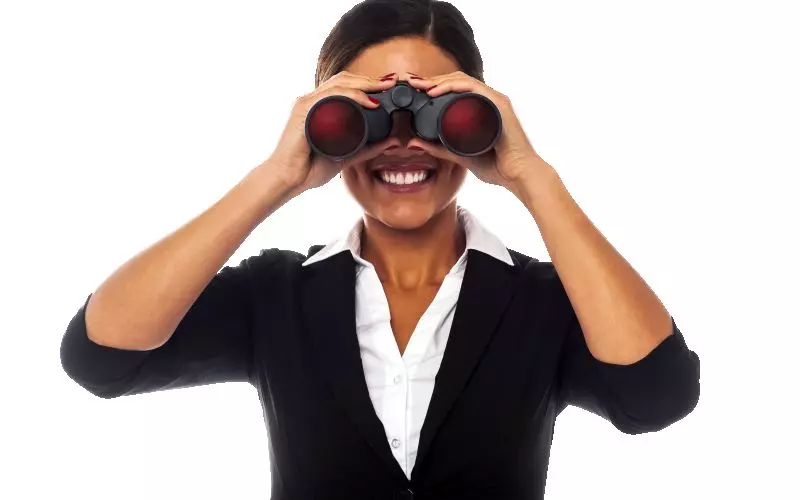 A smiling businesswoman looking through binoculars