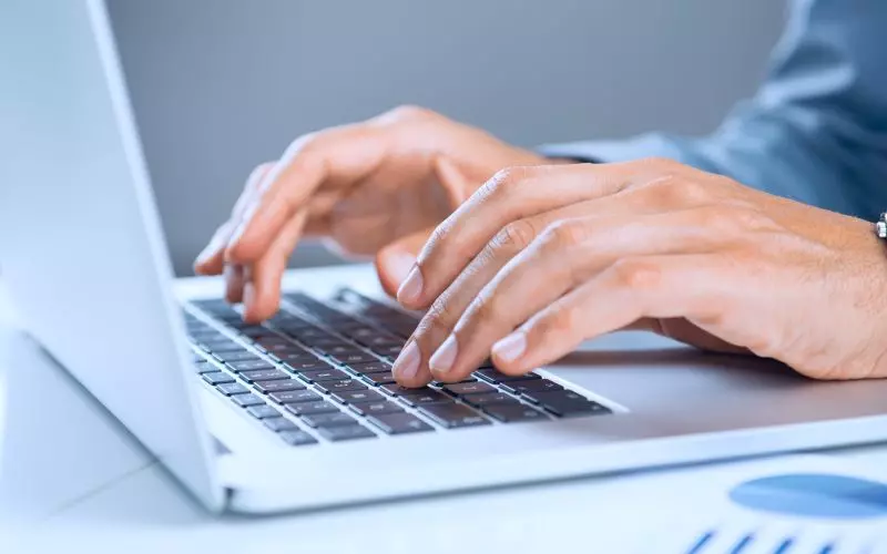 Hands typing on a white laptop