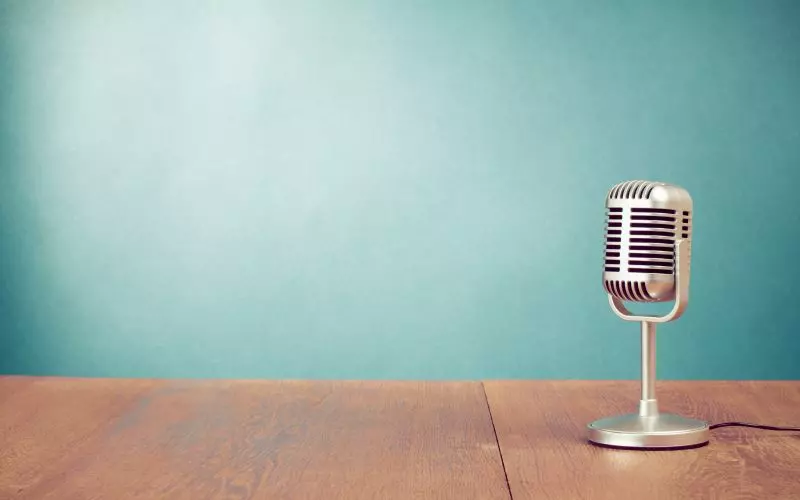 A vintage studio microphone on a wooden table against a teal wall