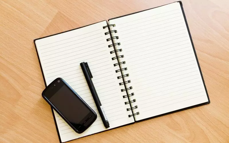 An open notebook with a pen and a phone on a desk