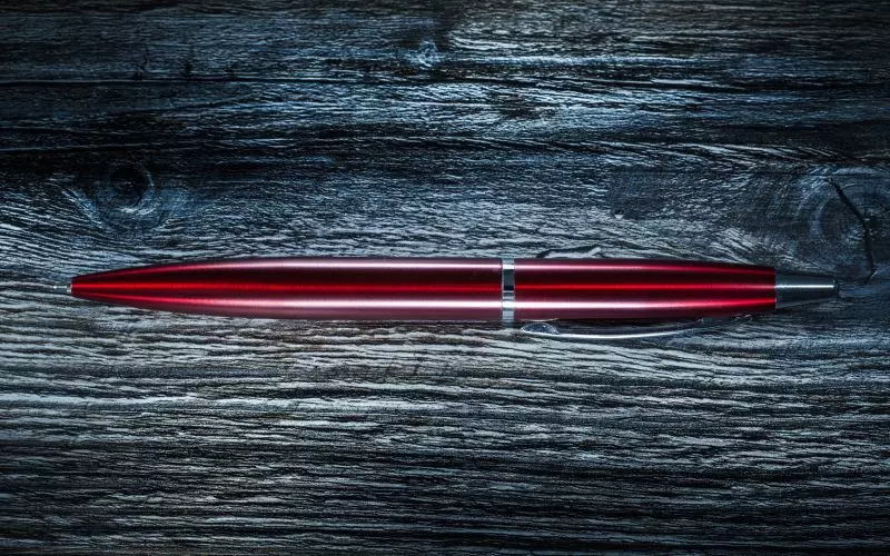 A single red pencil on dark wood
