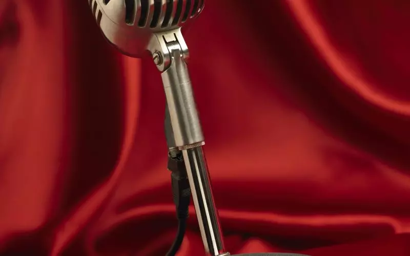 A vintage studio microphone in front of a red curtain