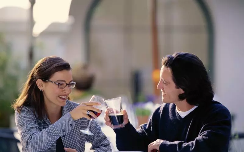 Two friends talking and laughing over drinks at an outdoor table